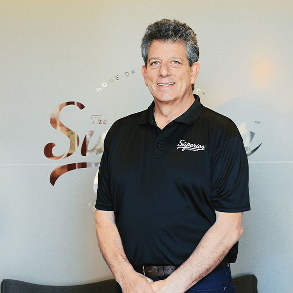 A man wearing a black superior dispensary shirt smiling in front of the superior sign