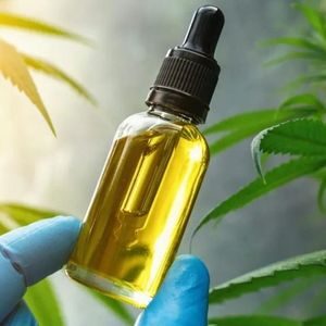 a small vial containing yellow oil and marijuana plants behind it